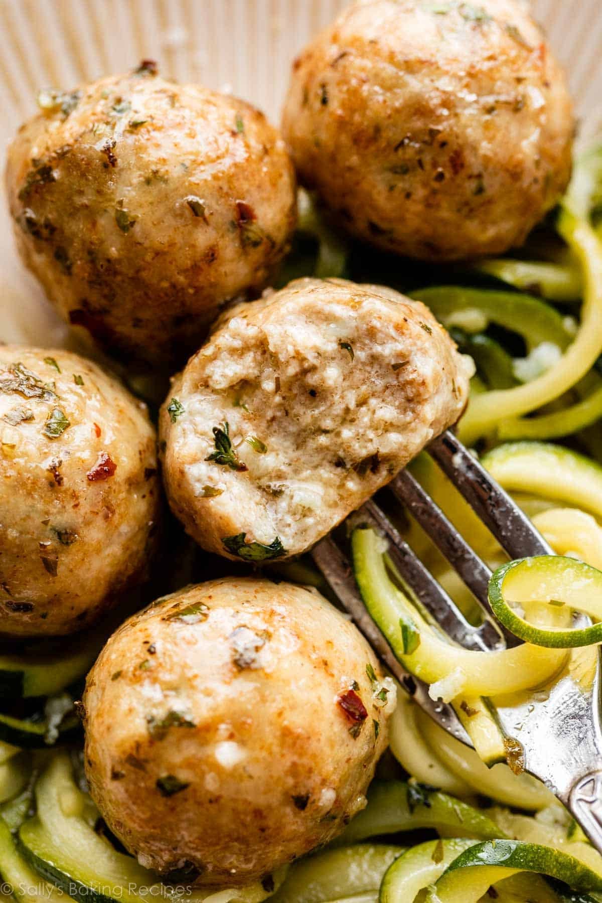 gros plan d'une boulette de poulet avec une bouchée prise, posée sur un lit de nouilles de courgette.