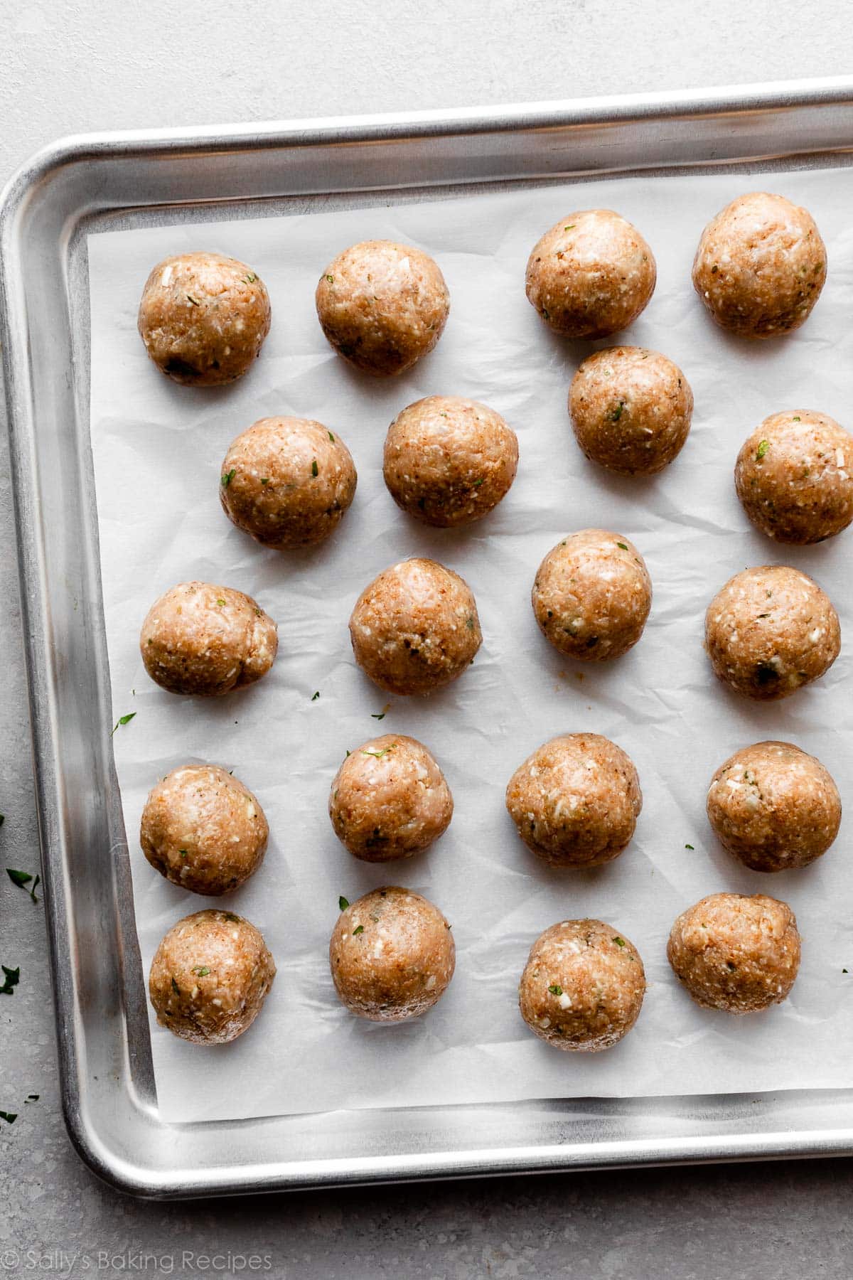 boulettes non cuites sur une plaque de cuisson recouverte de papier sulfurisé.