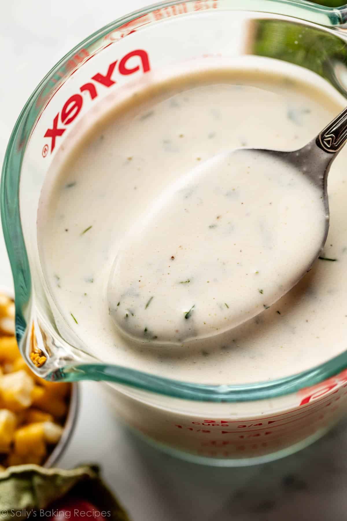 cuillère prélevant la vinaigrette aux herbes et lait ribot d'une tasse à mesurer transparente