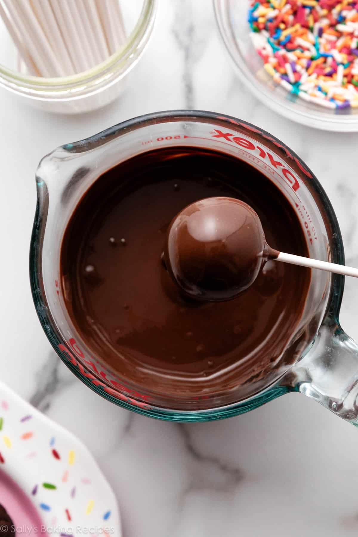 boule sur un bâton de sucette étant trempée dans du chocolat.