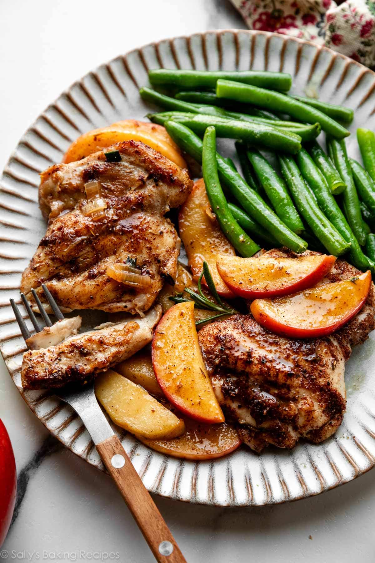 poulet au cidre de pomme et tranches de pommes avec haricots verts sur une assiette.