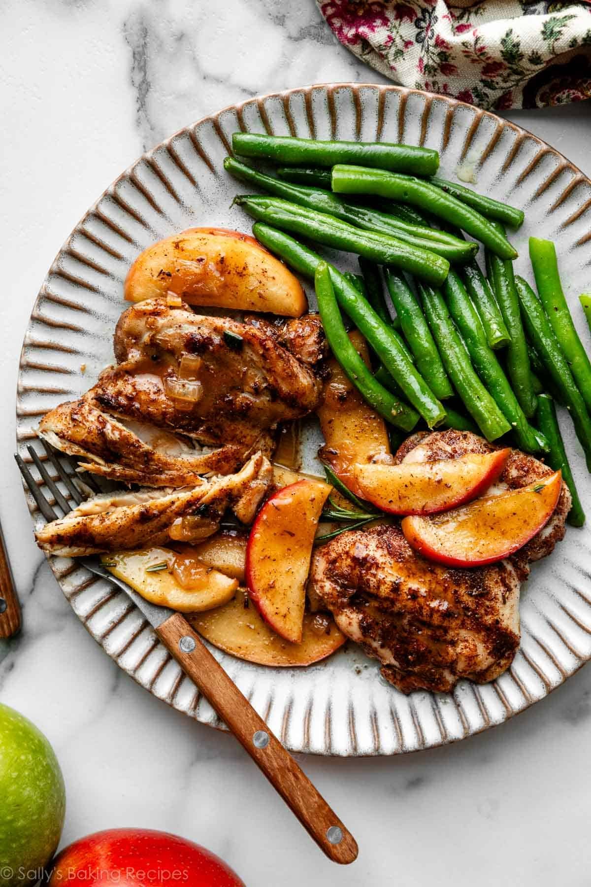 poulet au cidre de pomme et tranches de pommes avec des haricots verts sur une assiette.