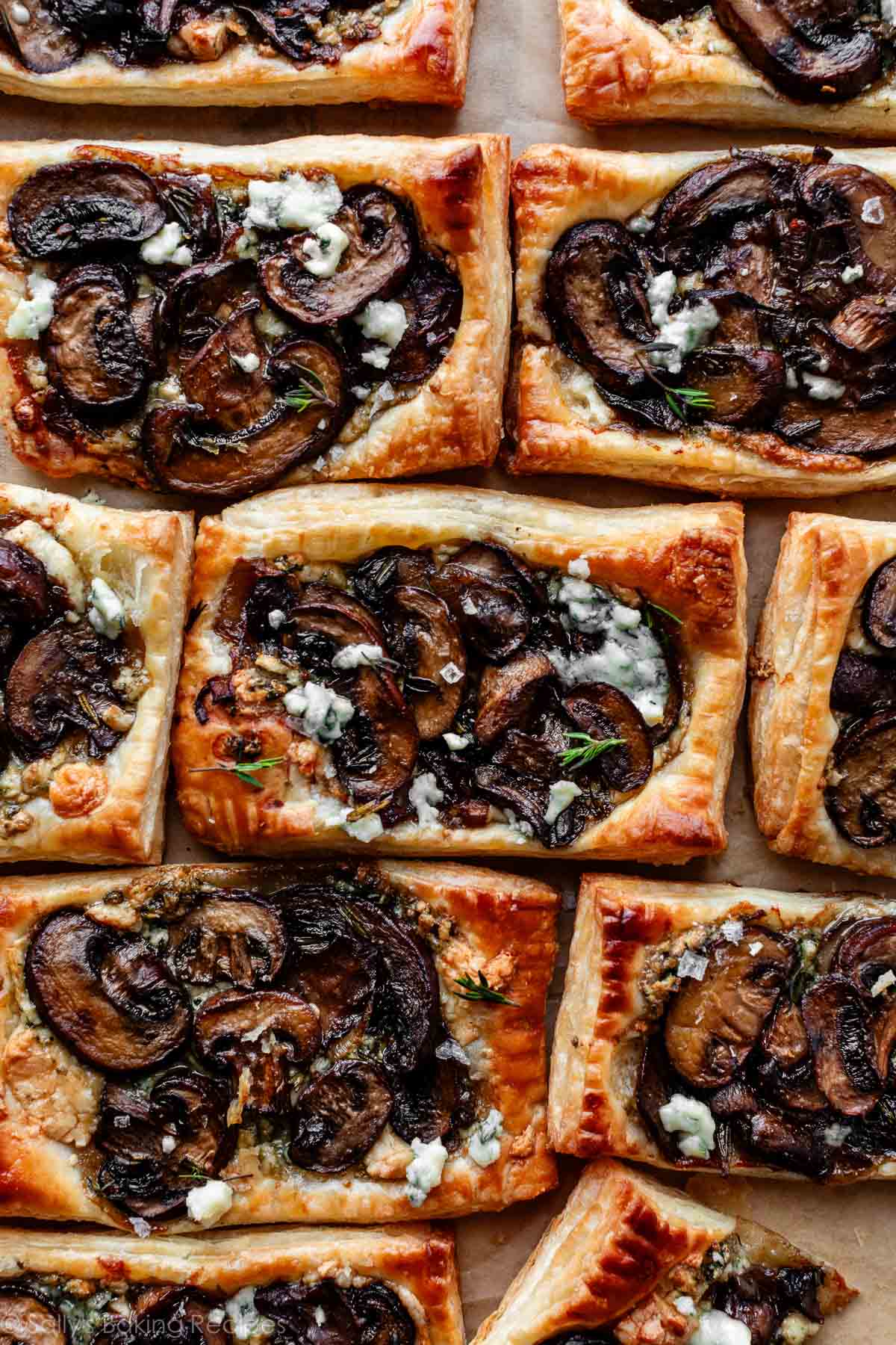 Tartes feuilletées aux champignons individuelles alignées sur du papier parchemin.