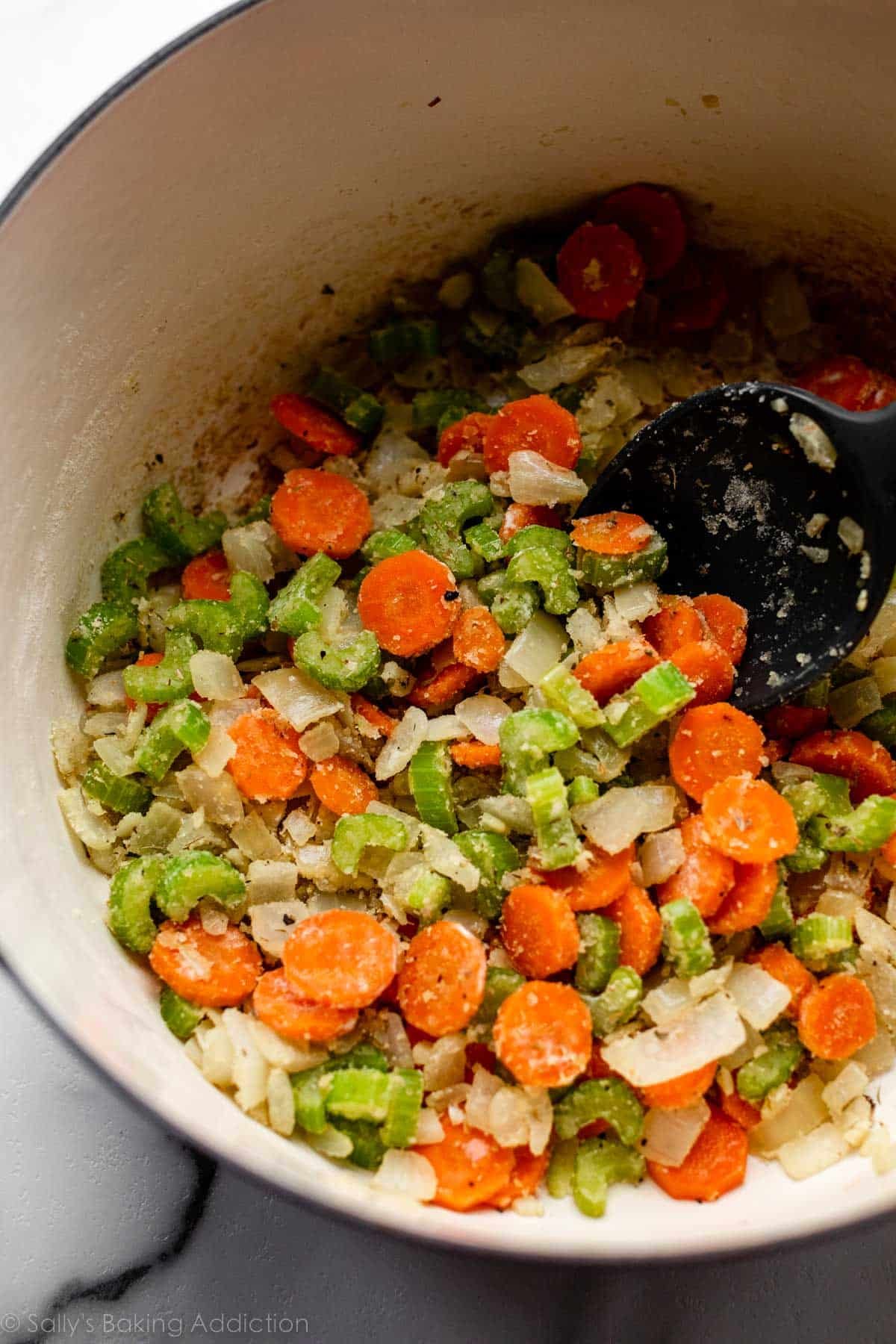 carottes, céleri et oignons mélangés avec des herbes dans une grande casserole.