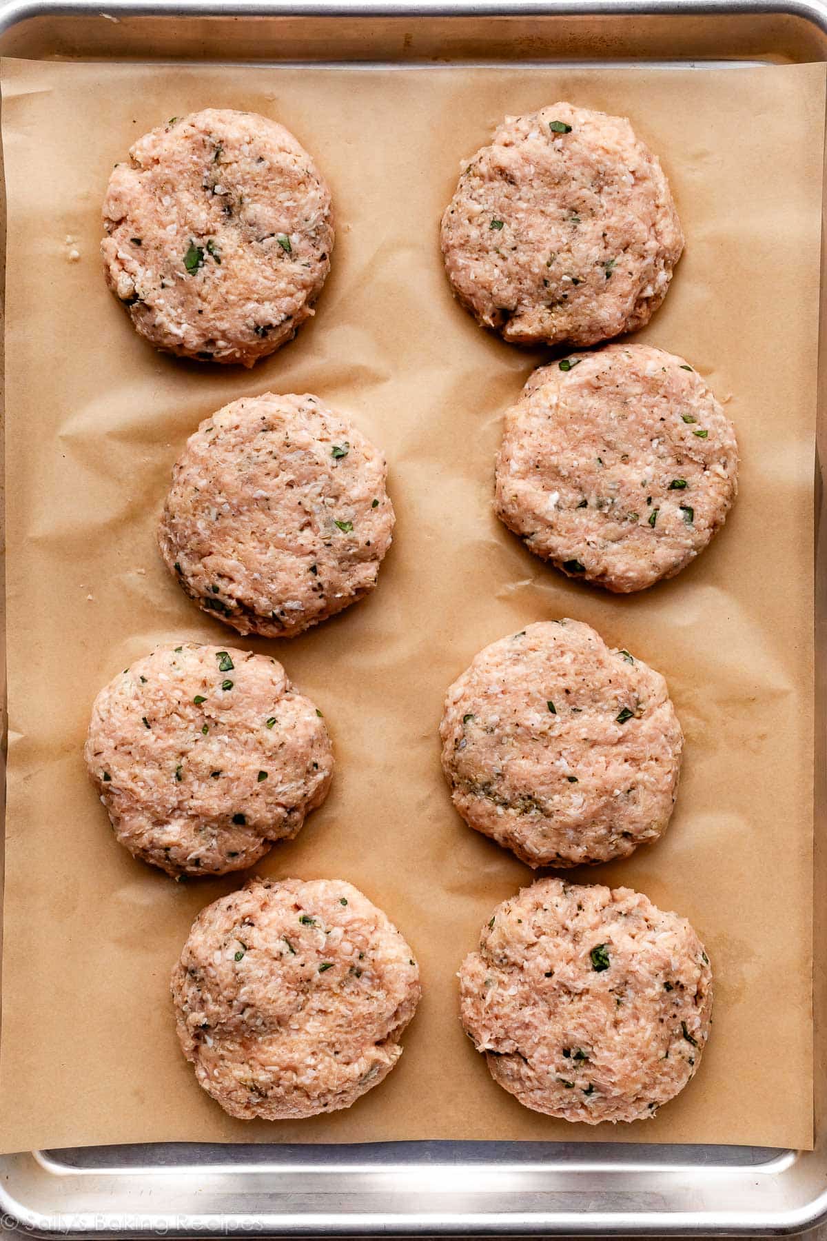 burgers de poulet formés sur une plaque de cuisson recouverte de papier sulfurisé.