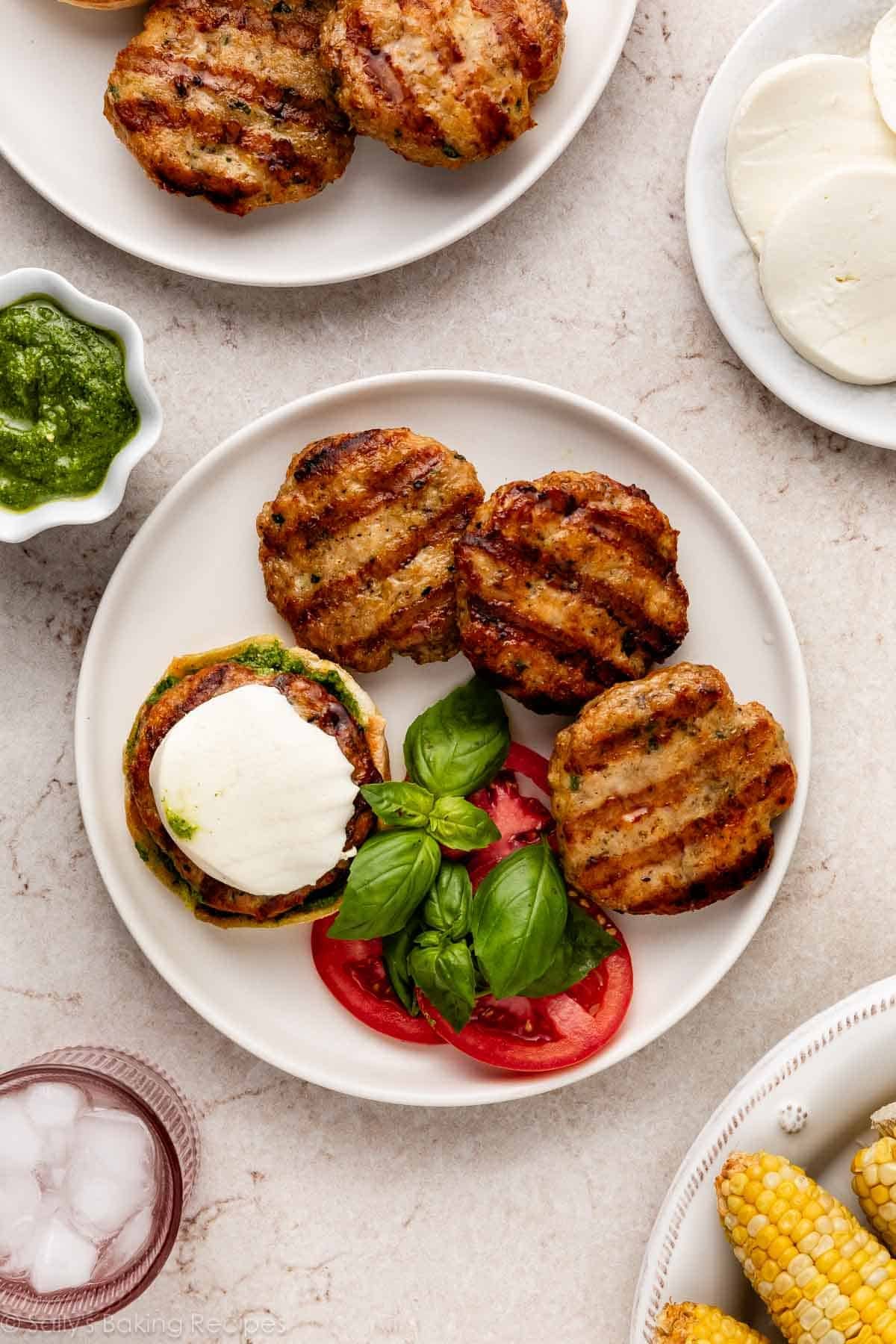 assiette de burgers avec marques de grill avec tomates et basilic frais, et un bol de pesto à côté.