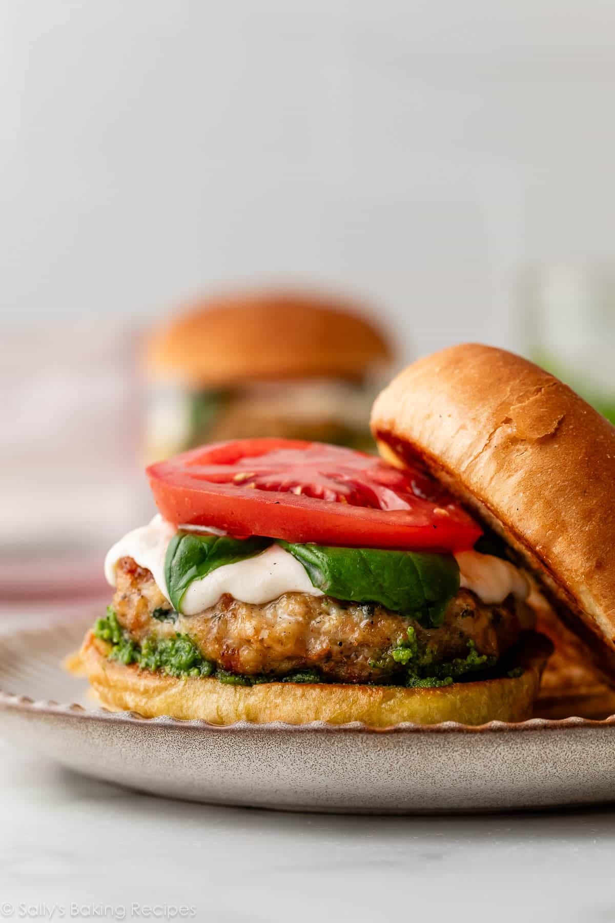 burger de poulet au pesto caprese ouvert sur un pain avec fromage mozzarella, basilic et tomate sur le dessus.