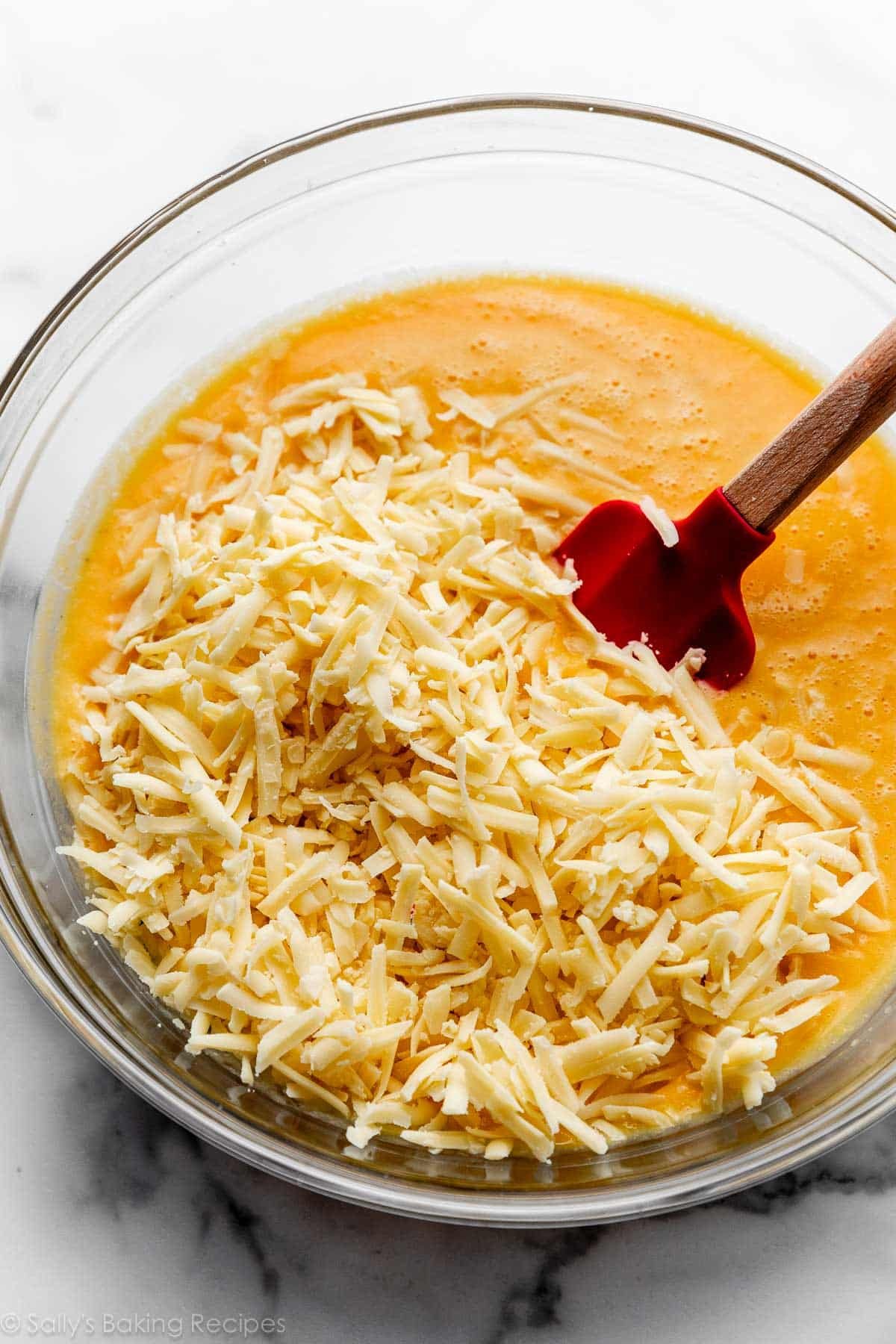 fromage gruyère râpé reposant sur la sauce orange dans un bol en verre avec une spatule rouge.