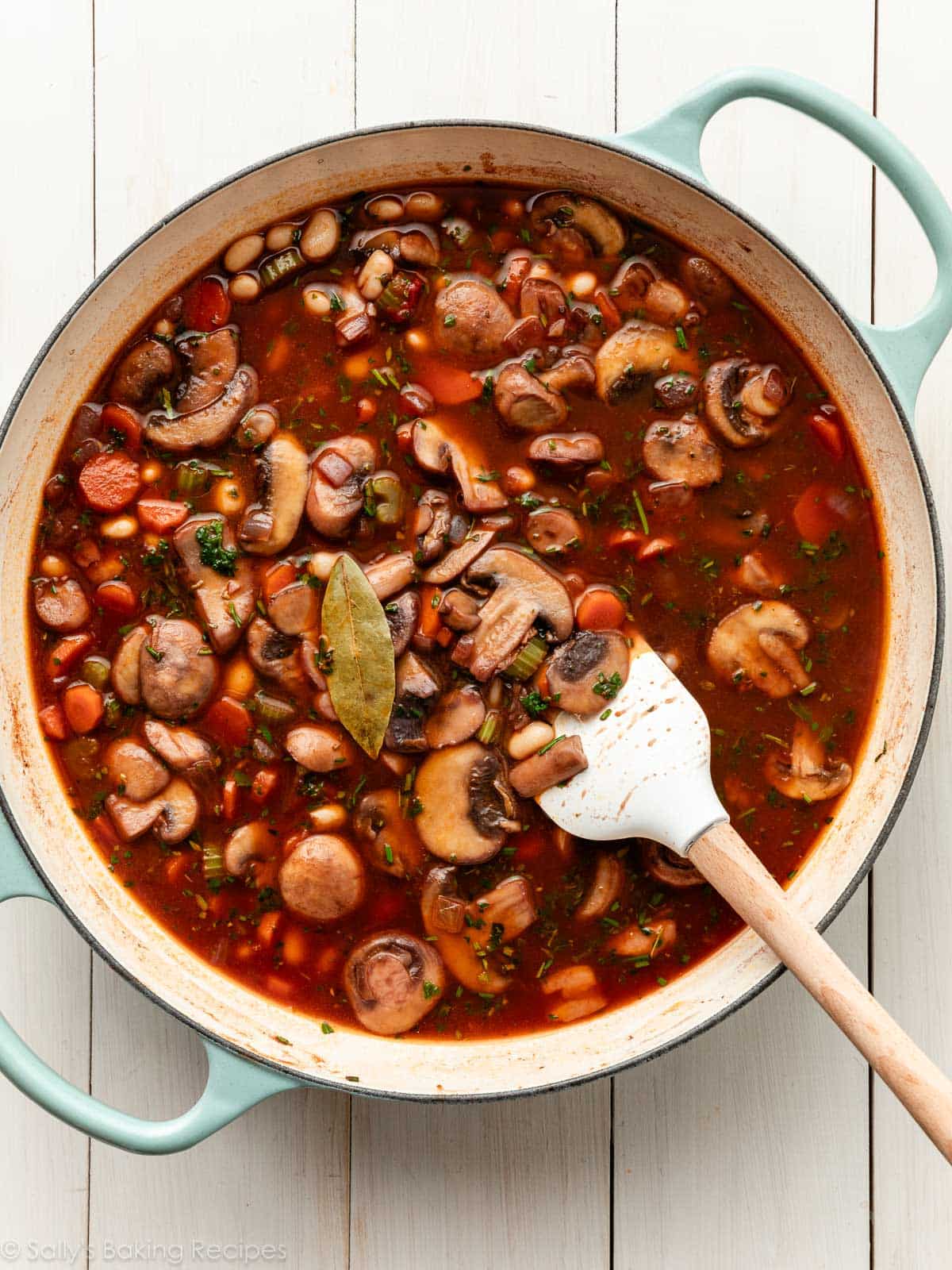 vin rouge et bouillon avec des légumes cuits mélangés et des herbes dans une poêle à main bleue.