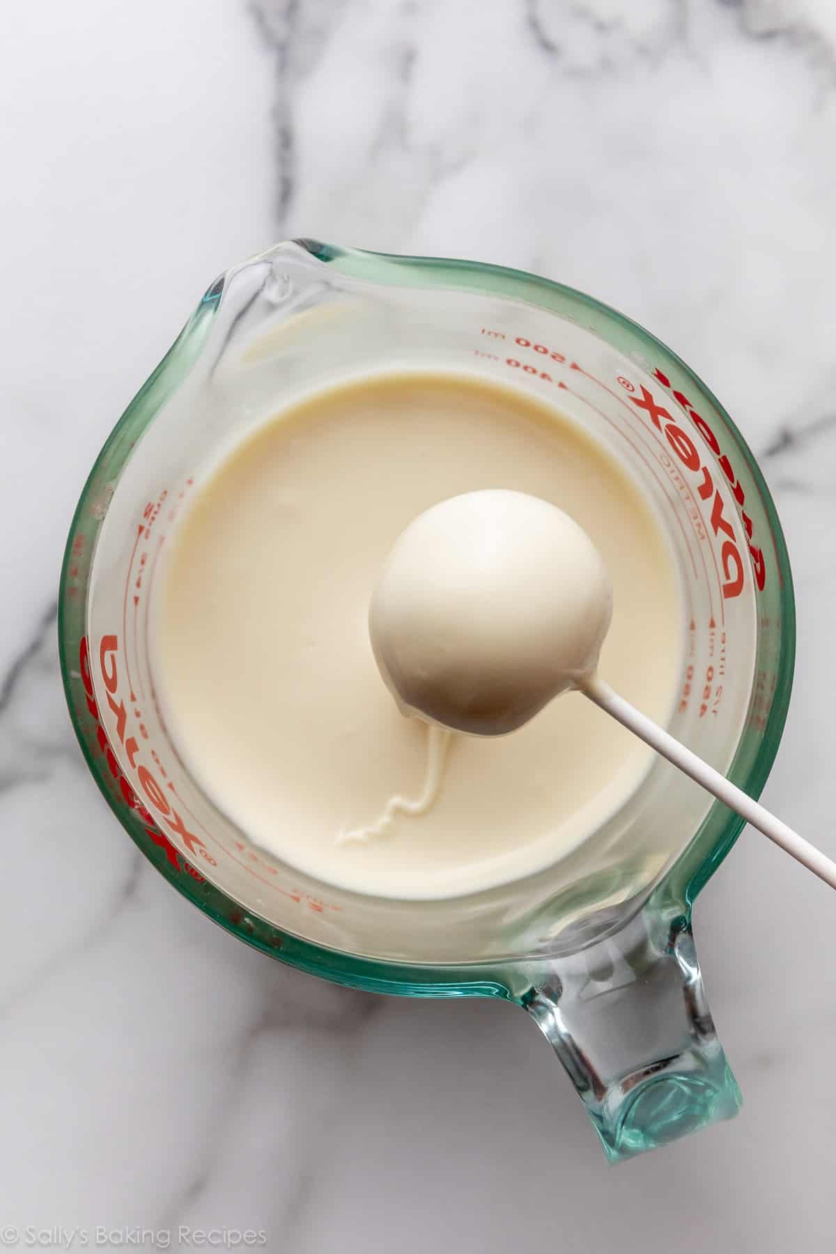 boule de gâteau sur un bâton de sucette enrobée de chocolat blanc.