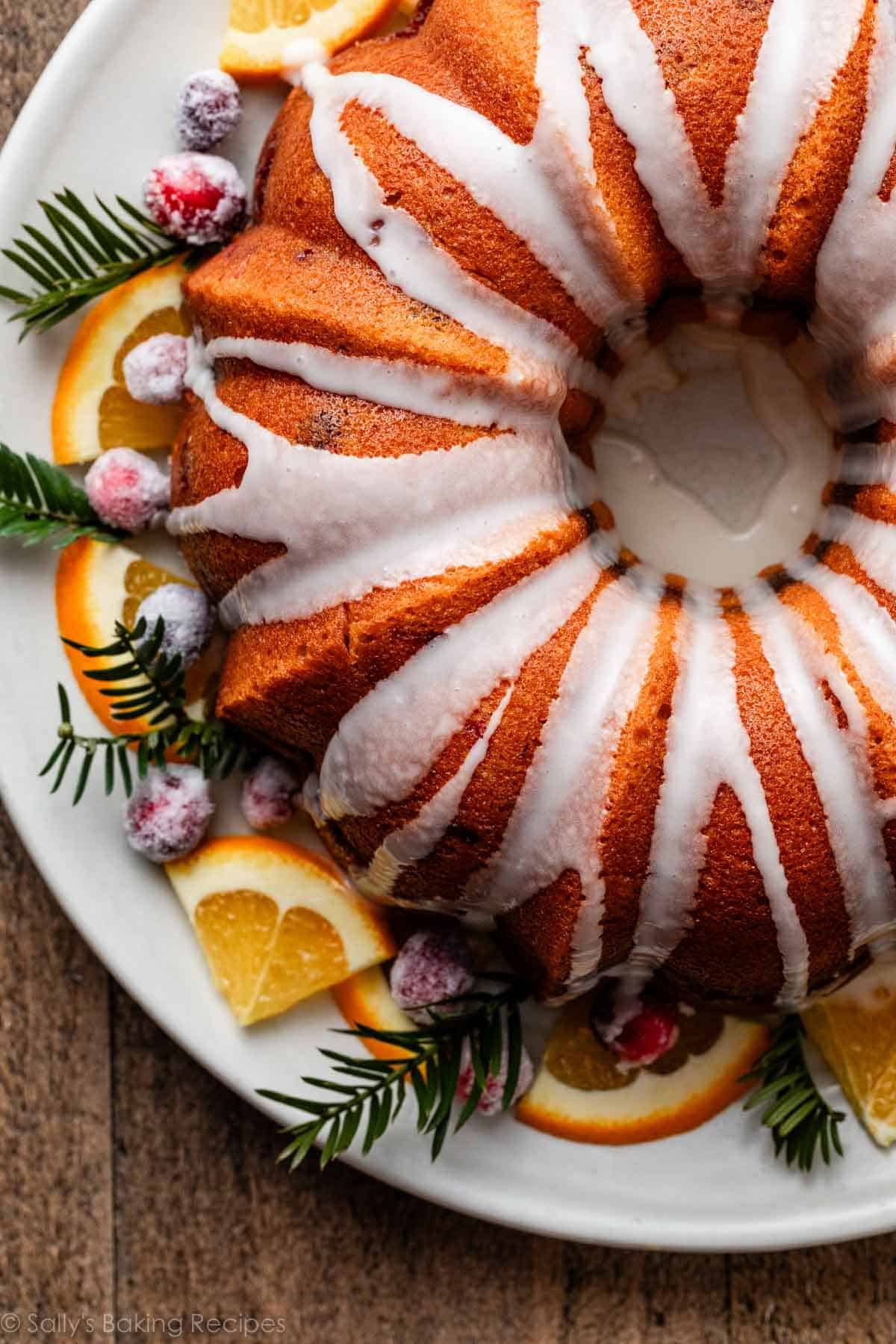 gâteau Bundt glacé à l'orange sur un plat avec des tranches d'orange et des pins frais.