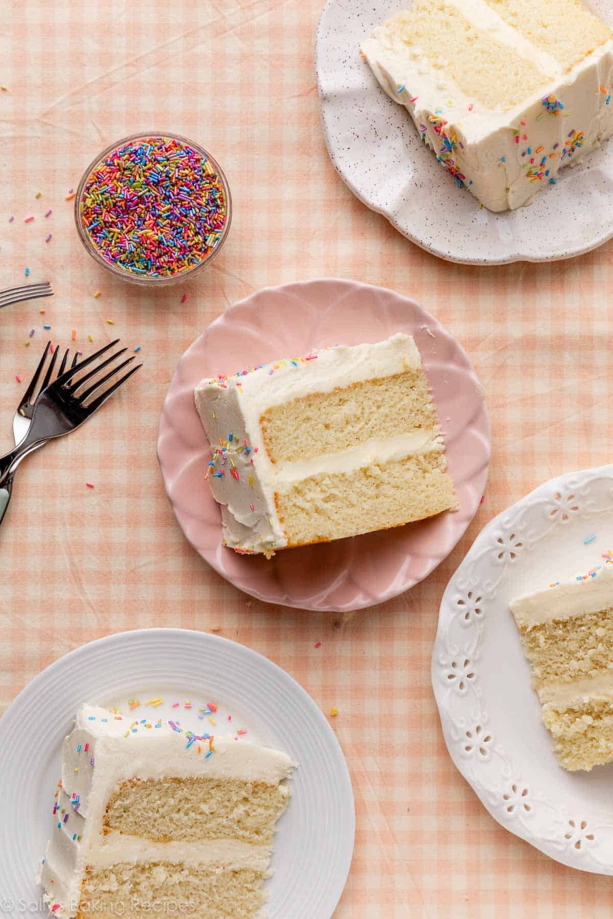 tranches de gâteau blanc avec glaçage à la vanille sur des assiettes assorties sur une nappe à carreaux.