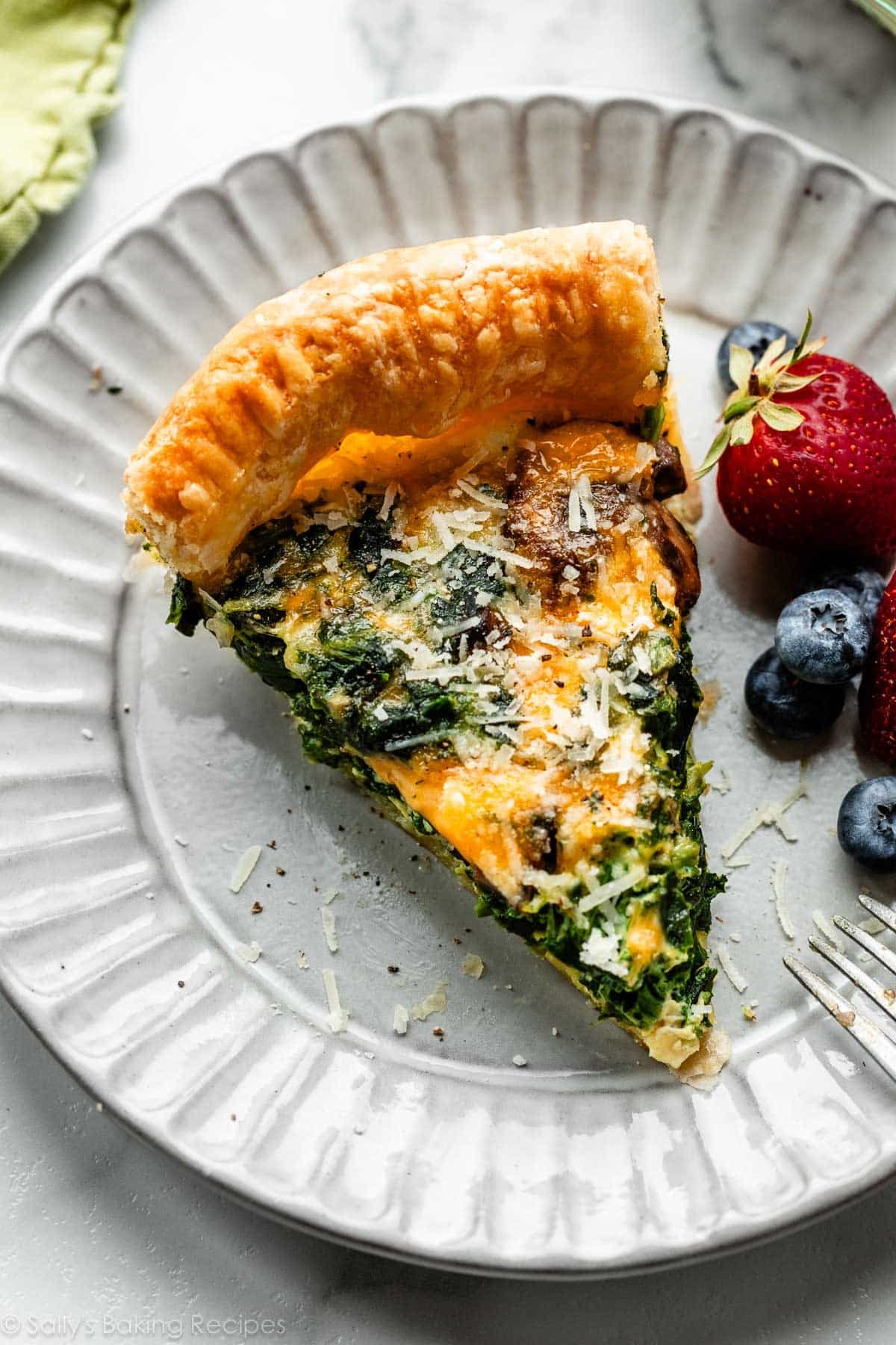 tranche de quiche aux épinards et au fromage sur une assiette grise avec des baies fraîches.