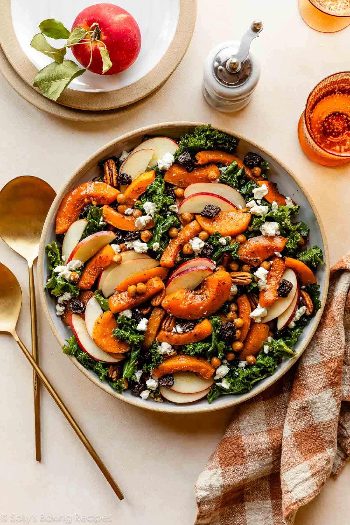 salade de courge butternut et kale dans un bol avec des pommes, des cerises séchées, du fromage de chèvre et des noix de pécan.