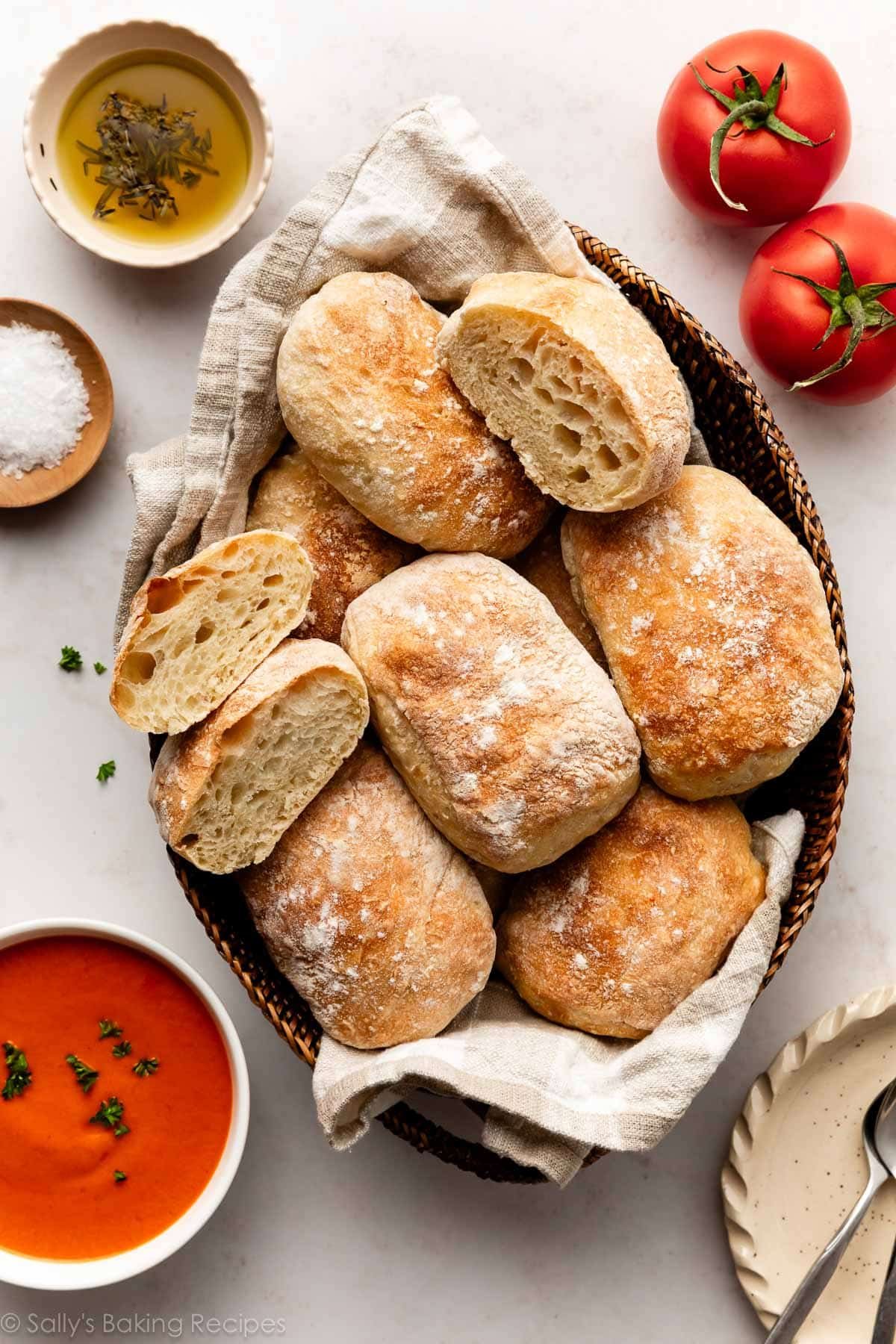 Pains ciabatta dans un panier avec des tomates, de la soupe et un petit bol d'huile d'olive à tremper à côté.