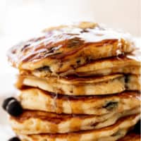 Une pile de pancakes aux myrtilles sur une assiette avec du sirop d'érable.