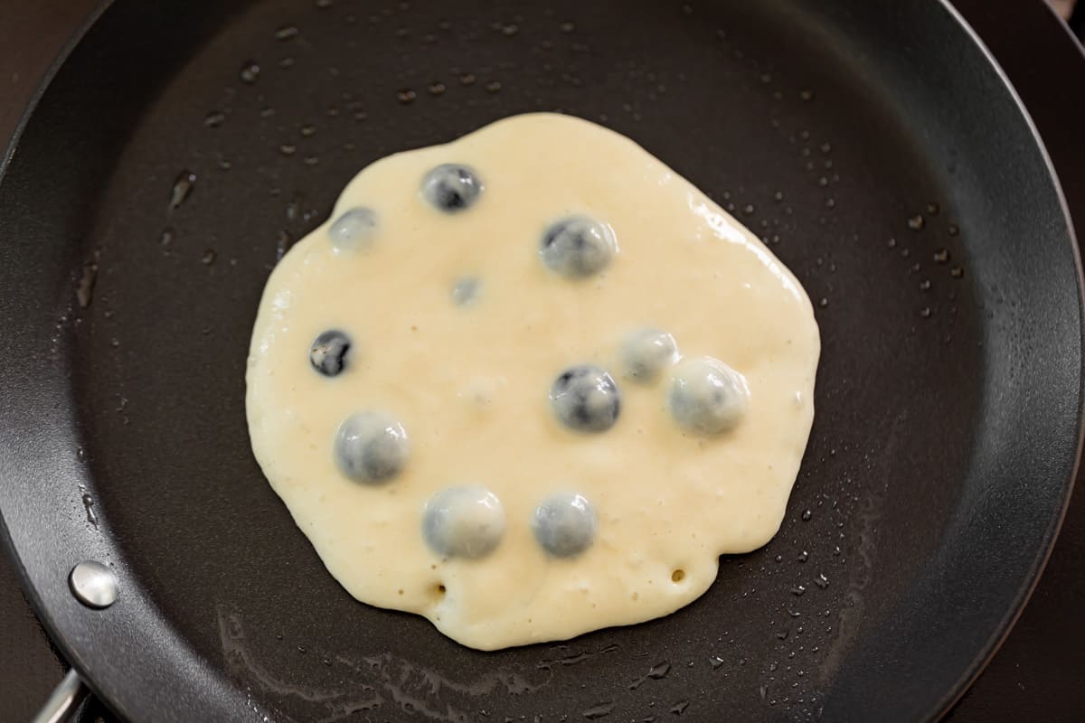 Pâte de pancakes aux myrtilles sur une poêle noire antiadhésive.