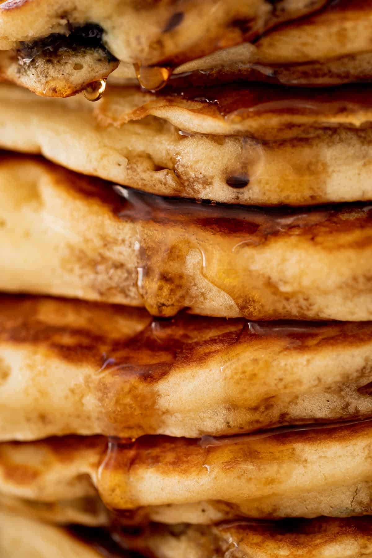 Gros plan sur une pile de pancakes aux myrtilles sur une assiette avec du sirop d'érable.