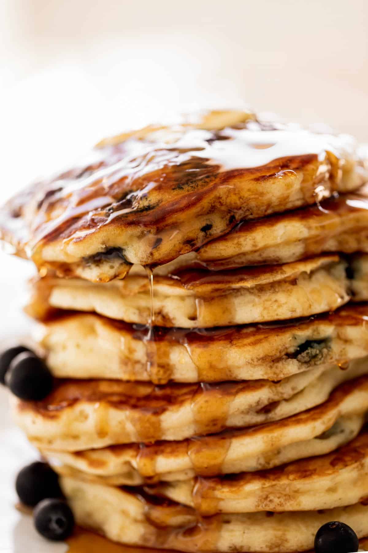 Une pile de pancakes aux myrtilles sur une assiette avec du sirop d'érable.