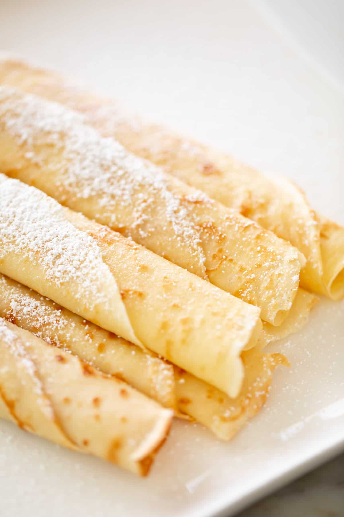 Vue aérienne de crêpes roulées sur une assiette avec du sucre glace.