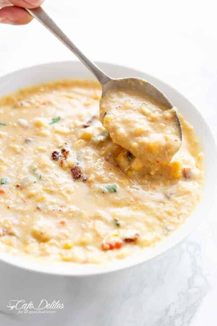 Un bol blanc de chowder au poulet et au maïs épais et crémeux. Une main remue le chowder avec une cuillère.