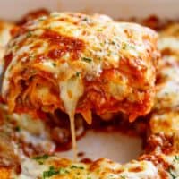 Une portion de lasagne est retirée d'un plat de cuisson blanc, avec un fil de fromage fondu s'étirant.