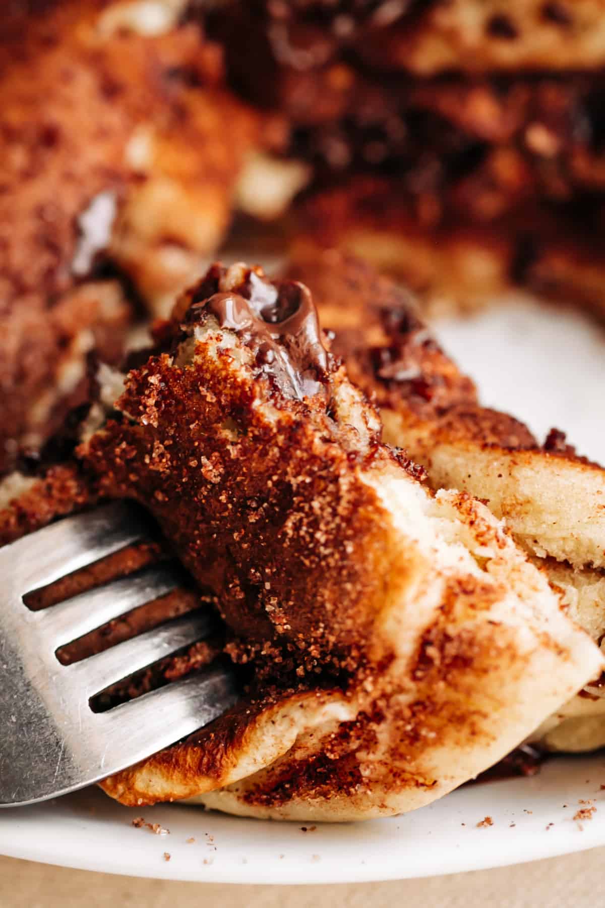 Gros plan d'une fourchette coincée dans une crêpe de churros fourrée au chocolat enrobée de sucre à la cannelle, avec un centre de chocolat fondu.