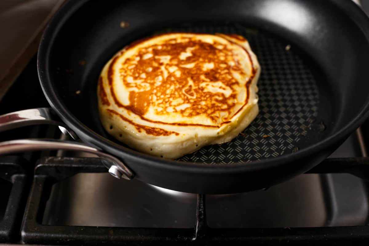 Crêpe épaisse et moelleuse dorée dans une poêle noire sur une cuisinière à feu doux après avoir été retournée pour cuire l'autre côté.