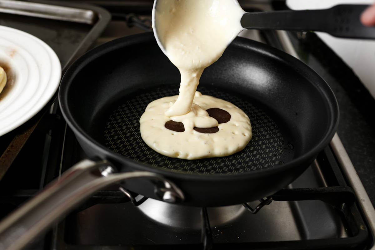 Louche versant plus de pâte sur la crêpe en train de cuire pour enfermer les boutons de chocolat au centre !