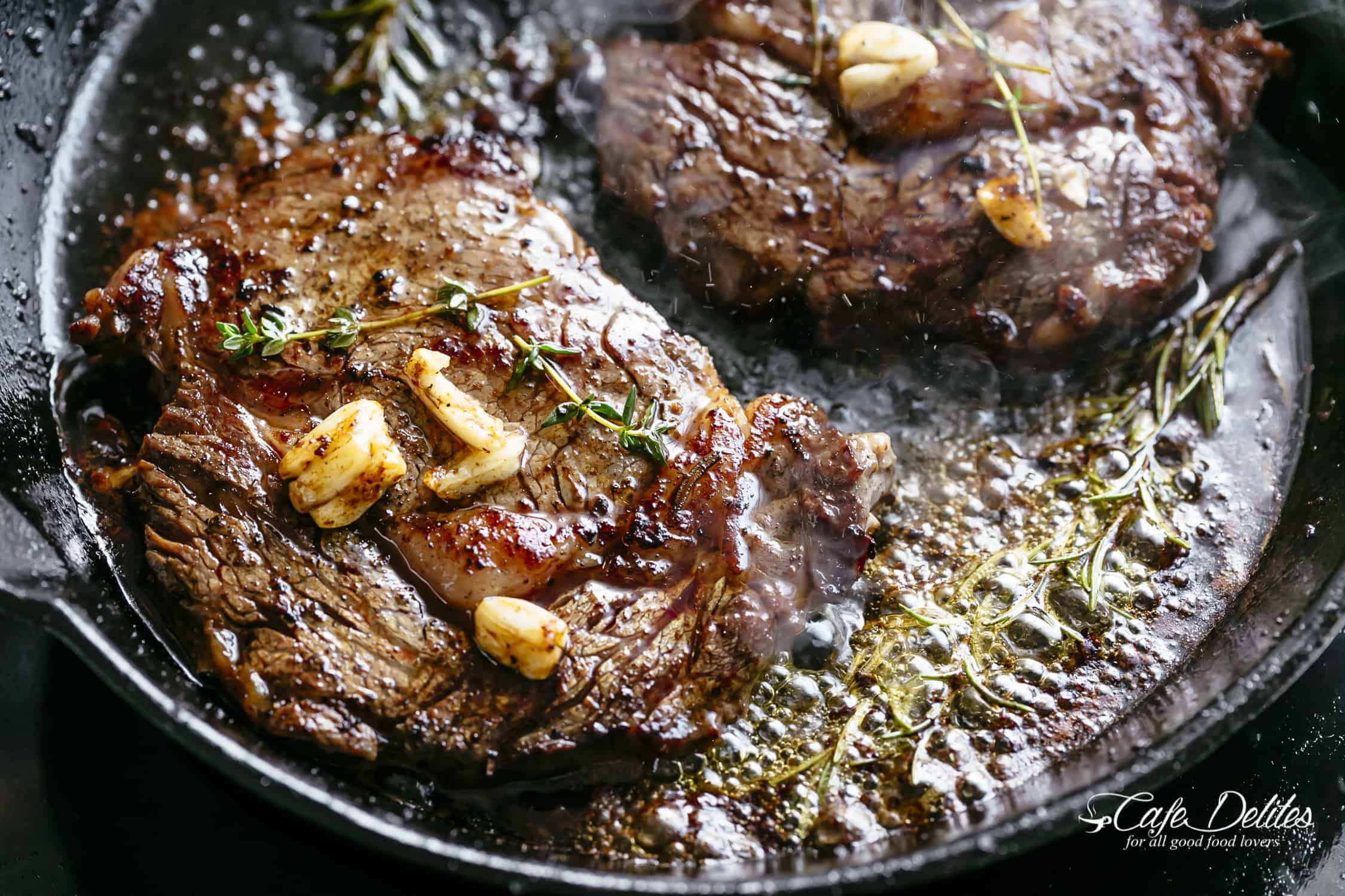 Gros plan sur des steaks crépitants couverts de beurre noisette et d'ail avec une branche de romarin mijotant dans une poêle!