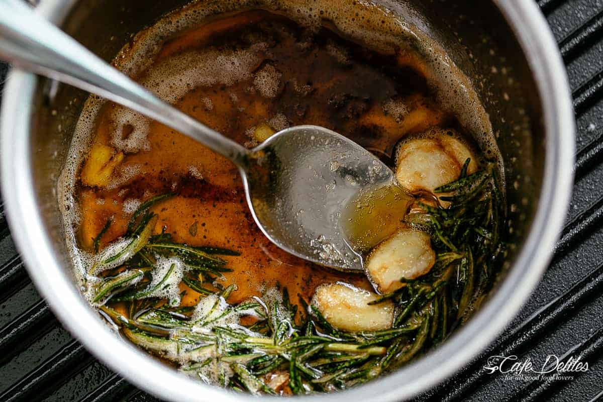 Image de beurre noisette avec des gousses d'ail et des brins de romarin dans une poêle en argent sur une poêle à grill.