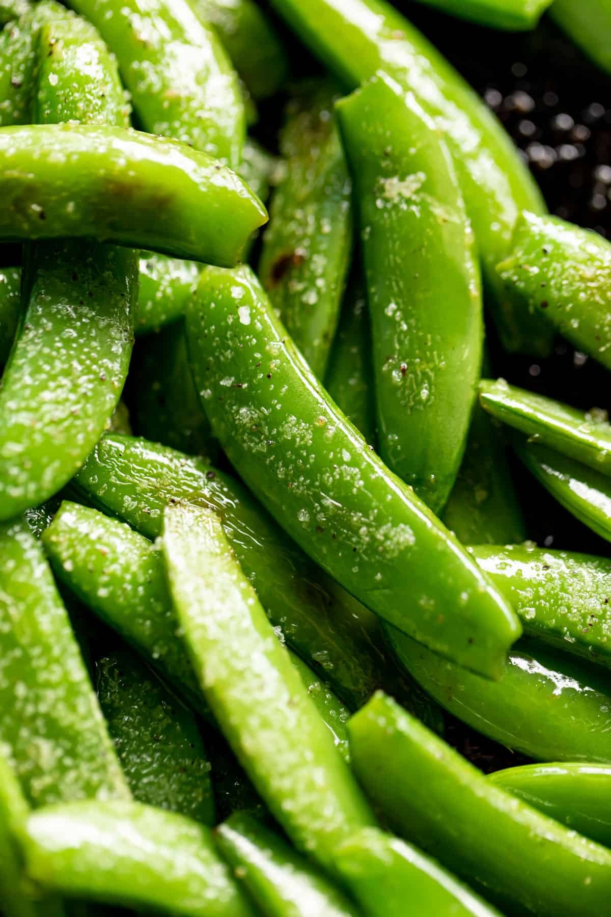 Gros plan sur les pois sucrés verts, sautés dans une poêle noire, saupoudrés de sel gros.