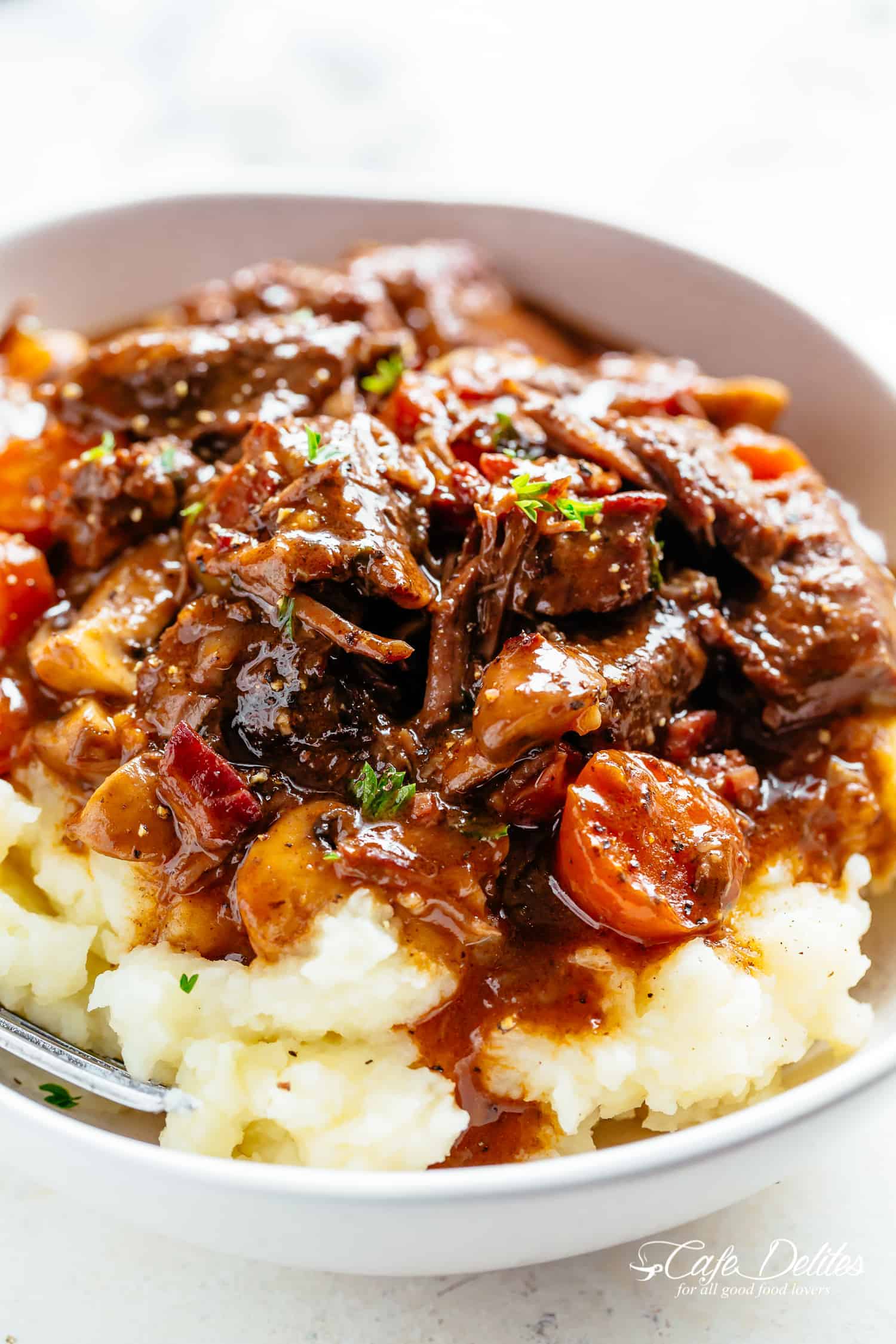 Boeuf Bourgignon servi sur de la purée de pommes de terre avec de la sauce dans un bol blanc avec une fourchette.