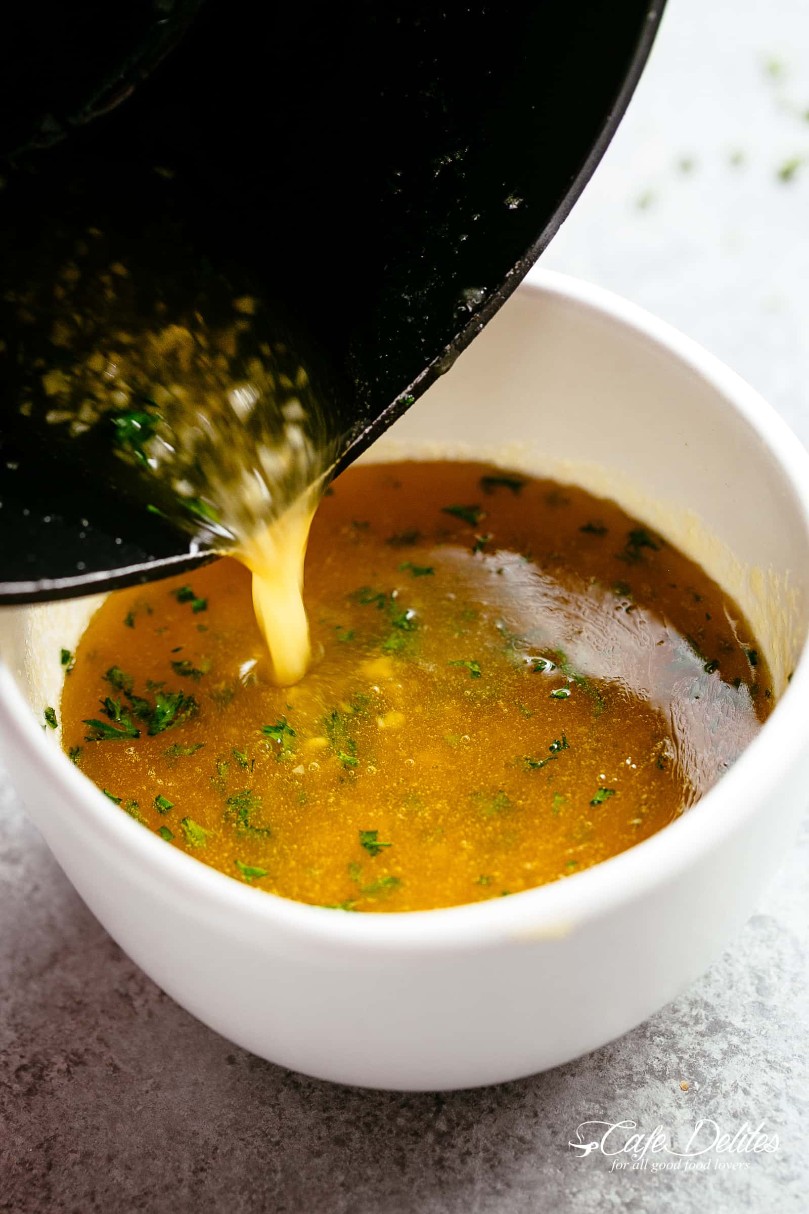 Sauce au beurre d'ail et au miel chaude et épicée coulant d'une casserole noire dans une petite tasse de sauce blanche avec de petits morceaux d'ail et de persil.