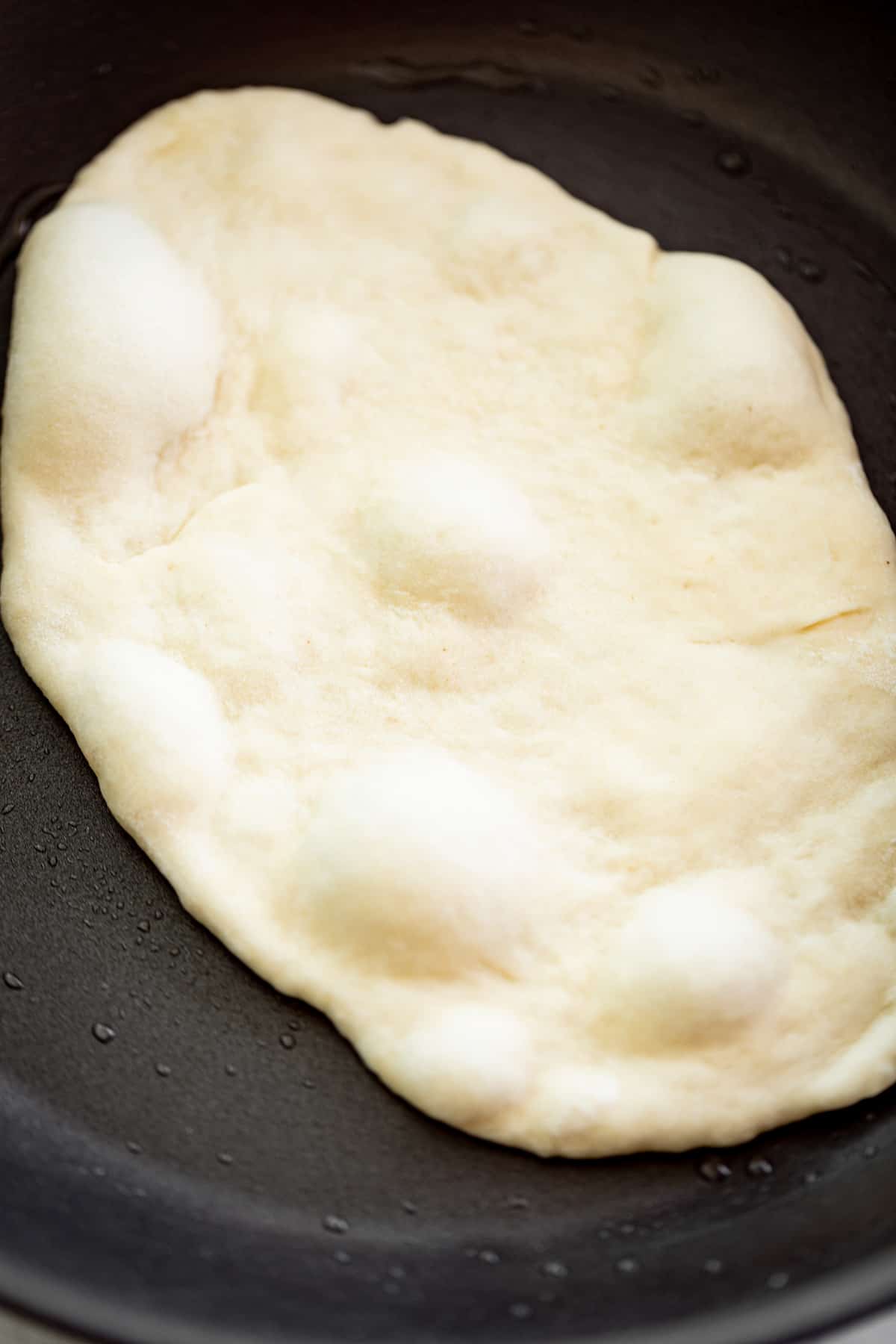 Image d'un pain naan à l'ail en train de cuire dans une poêle noire.