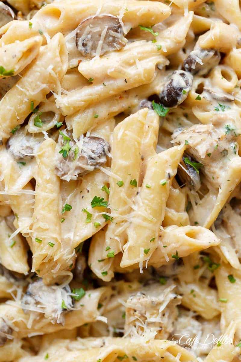 Gros plan d'articles de viande saisie mélangés à ce plat avec de l'ail, des champignons et du fromage parmesan avec des herbes fraîches par-dessus.