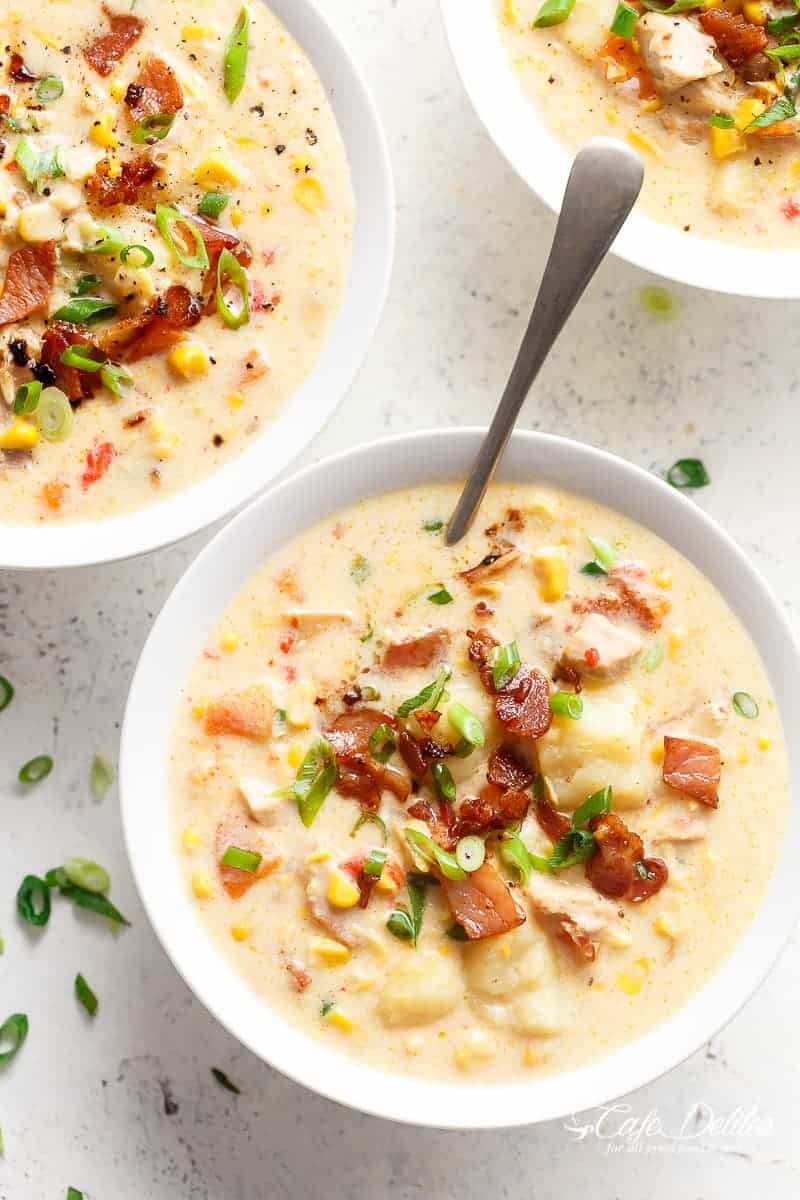 Trois bols de chowder au poulet et au maïs saupoudrés de bacon et d'oignons nouveaux hachés avec des cuillères.