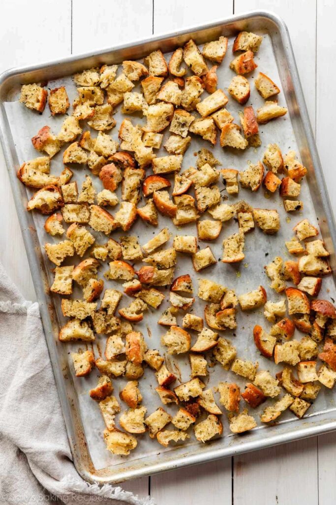 homemade baked croutons spread on lined baking sheet.