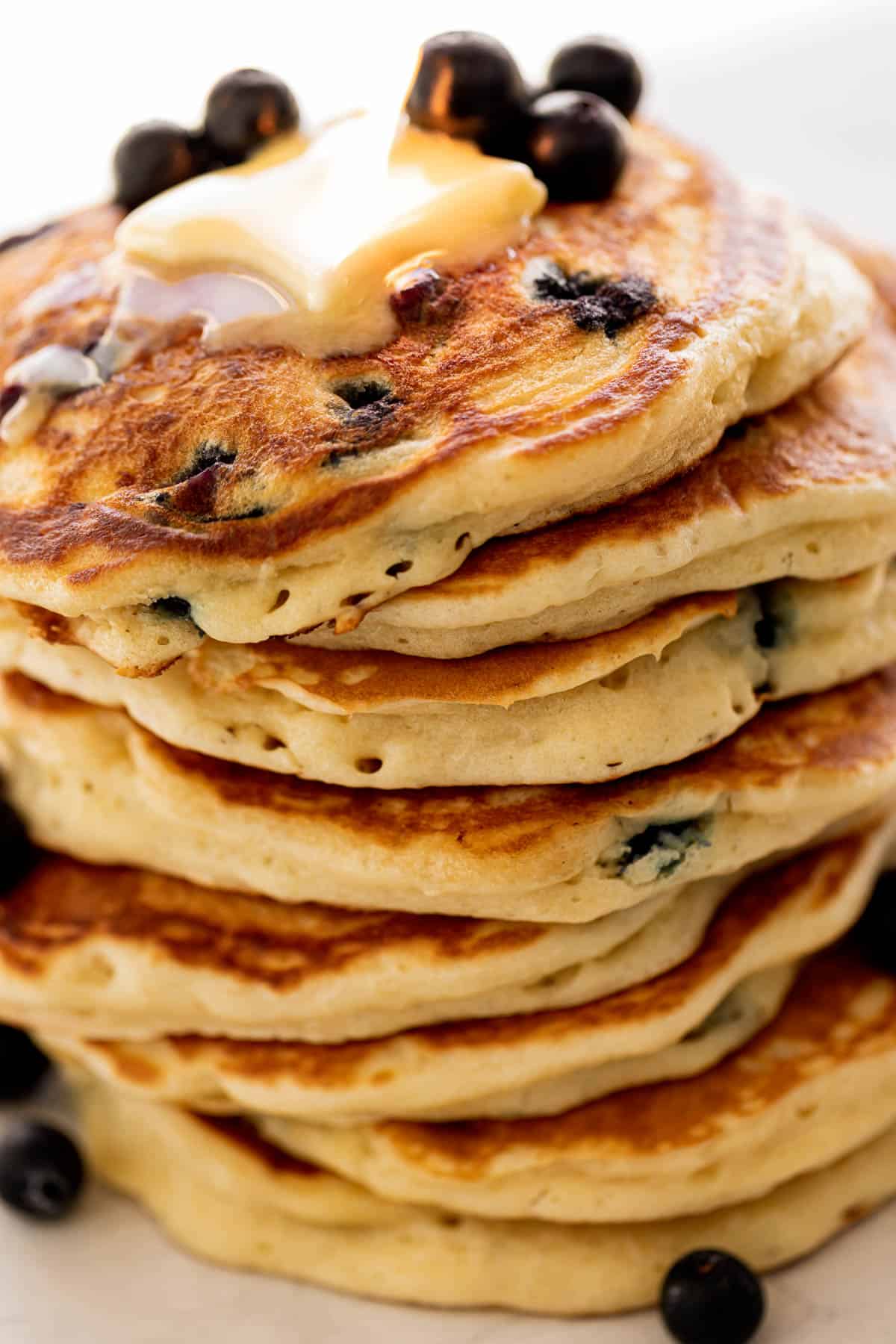 Idée de vue d'une pile de pancakes aux myrtilles sur une assiette garnie de myrtilles fraîches et de beurre fondu.