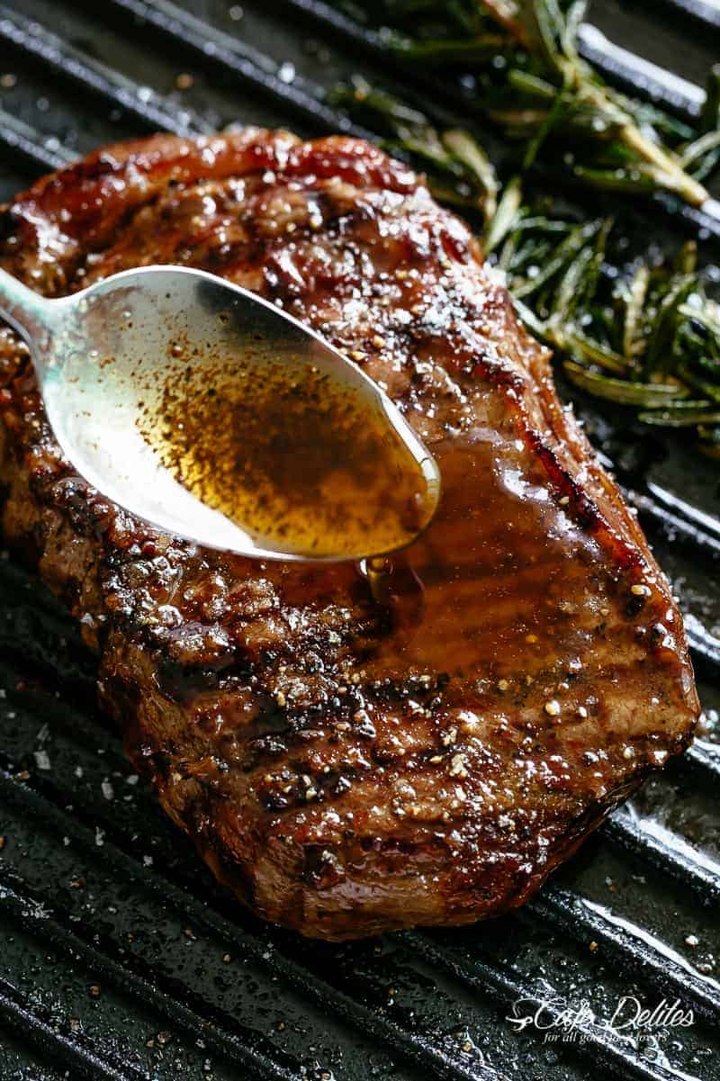 Cuillère en argent drizzled garlic browned butter over Juicy steak with rosemary on a black grill.