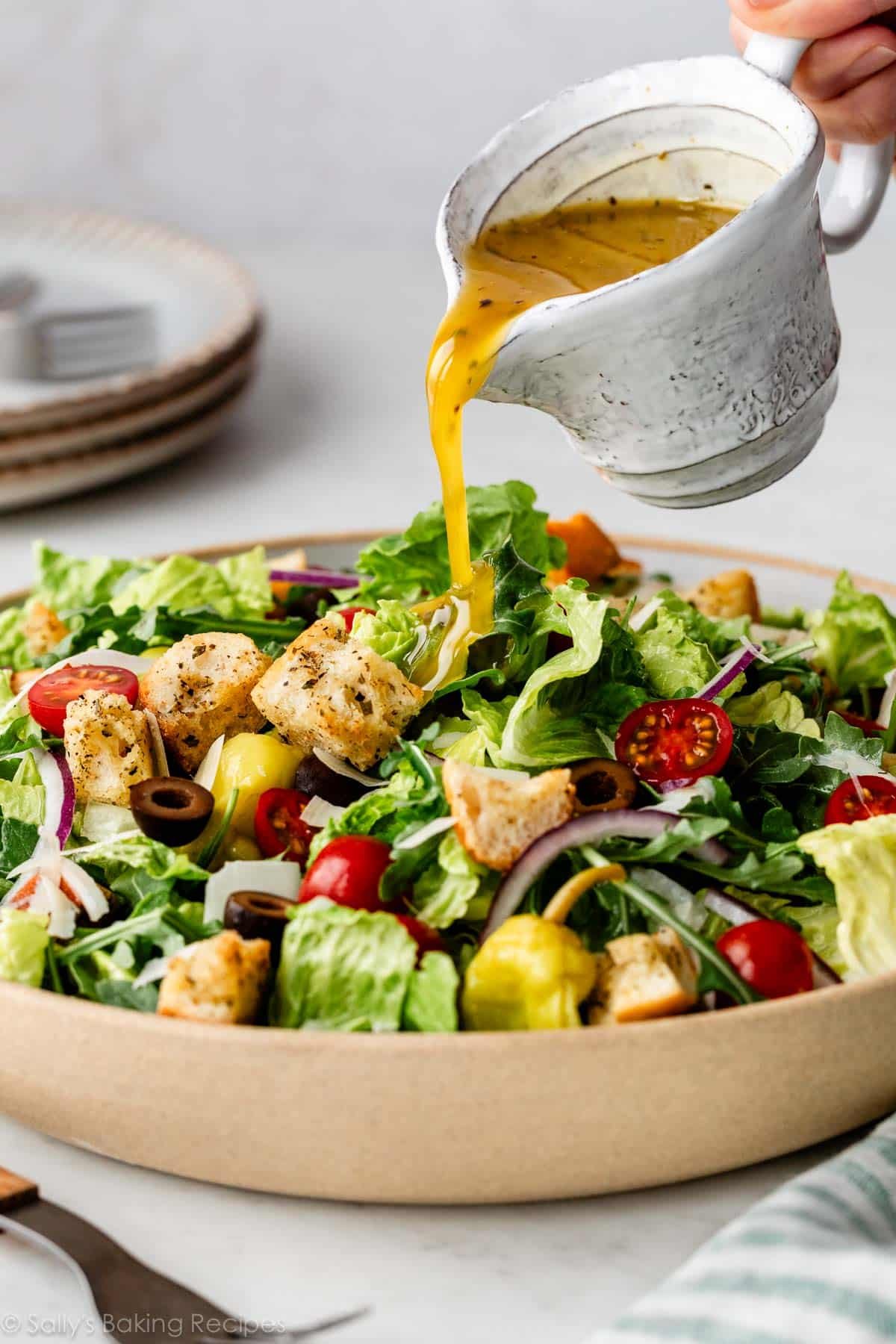 pouring homemade Italian dressing over a green salad.