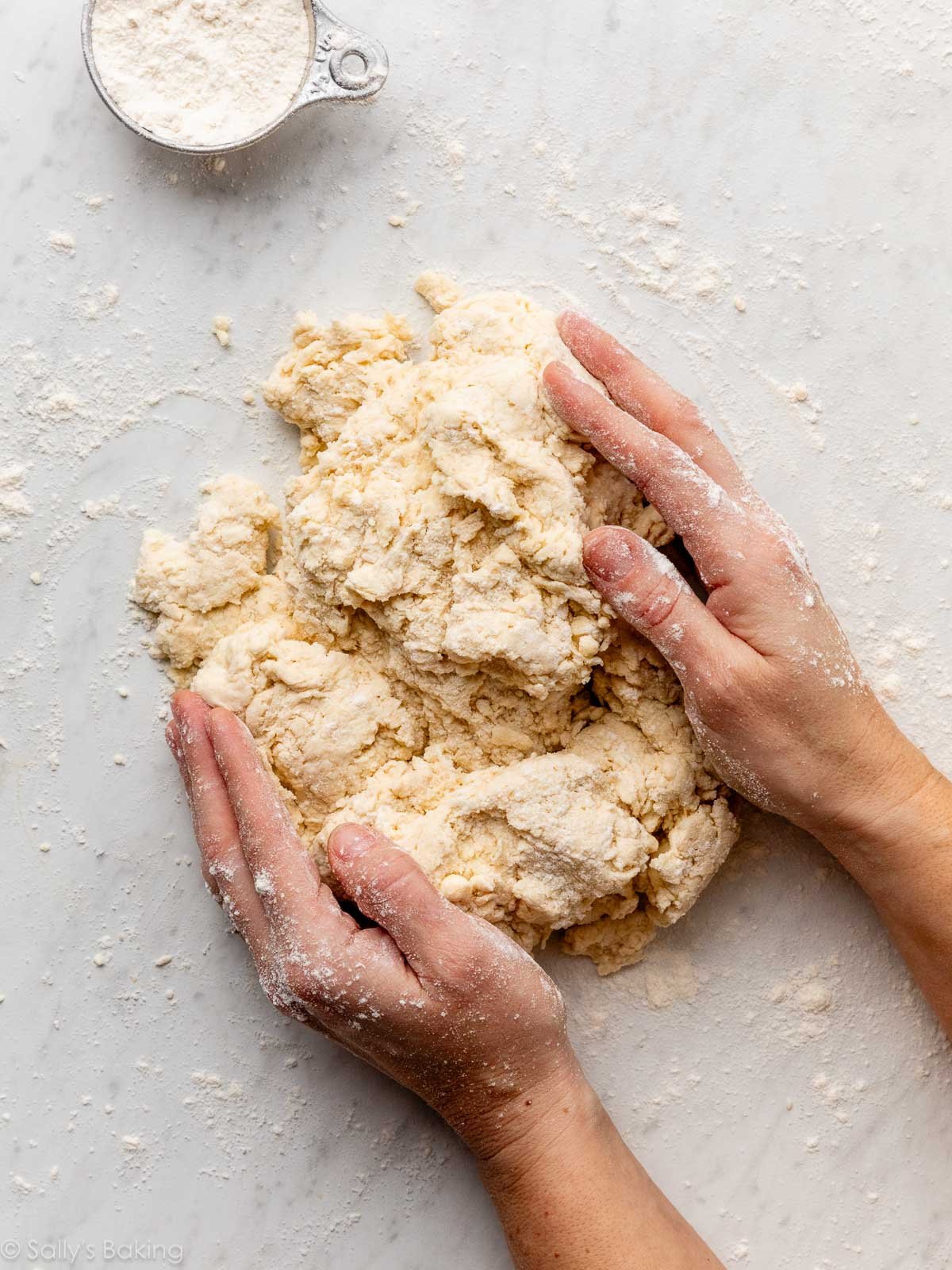 mains ramassant la pâte sur une surface en marbre.