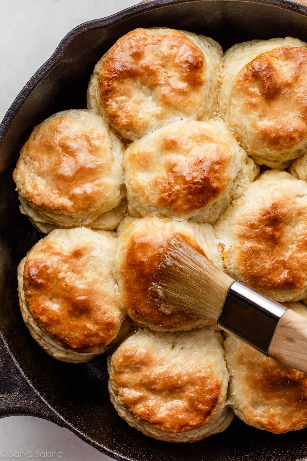 biscuits faits maison dans une poêle en fonte étant badigeonnés de beurre fondu.