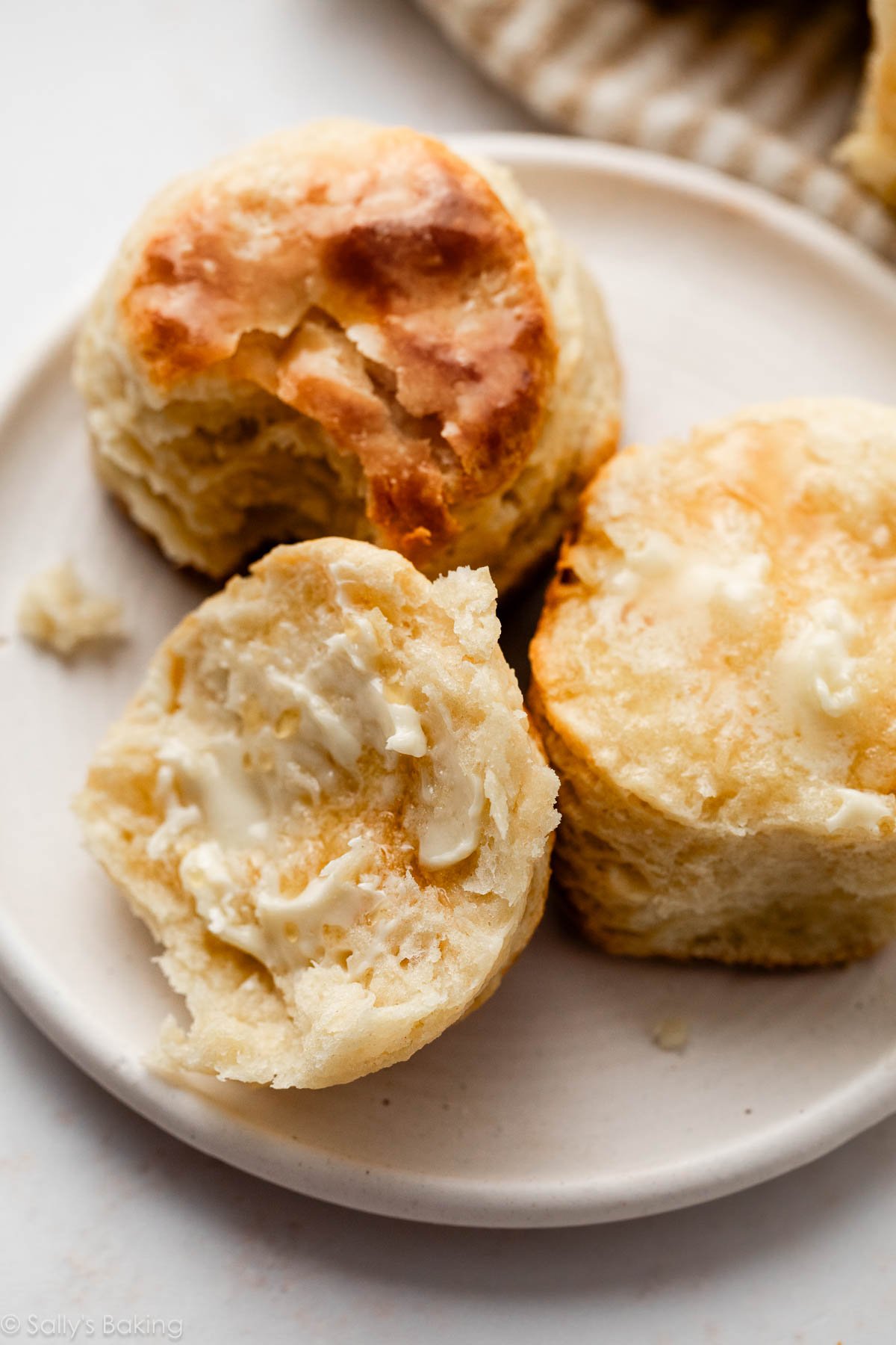 biscuits faits maison coupés en deux avec du beurre sur une assiette blanche.