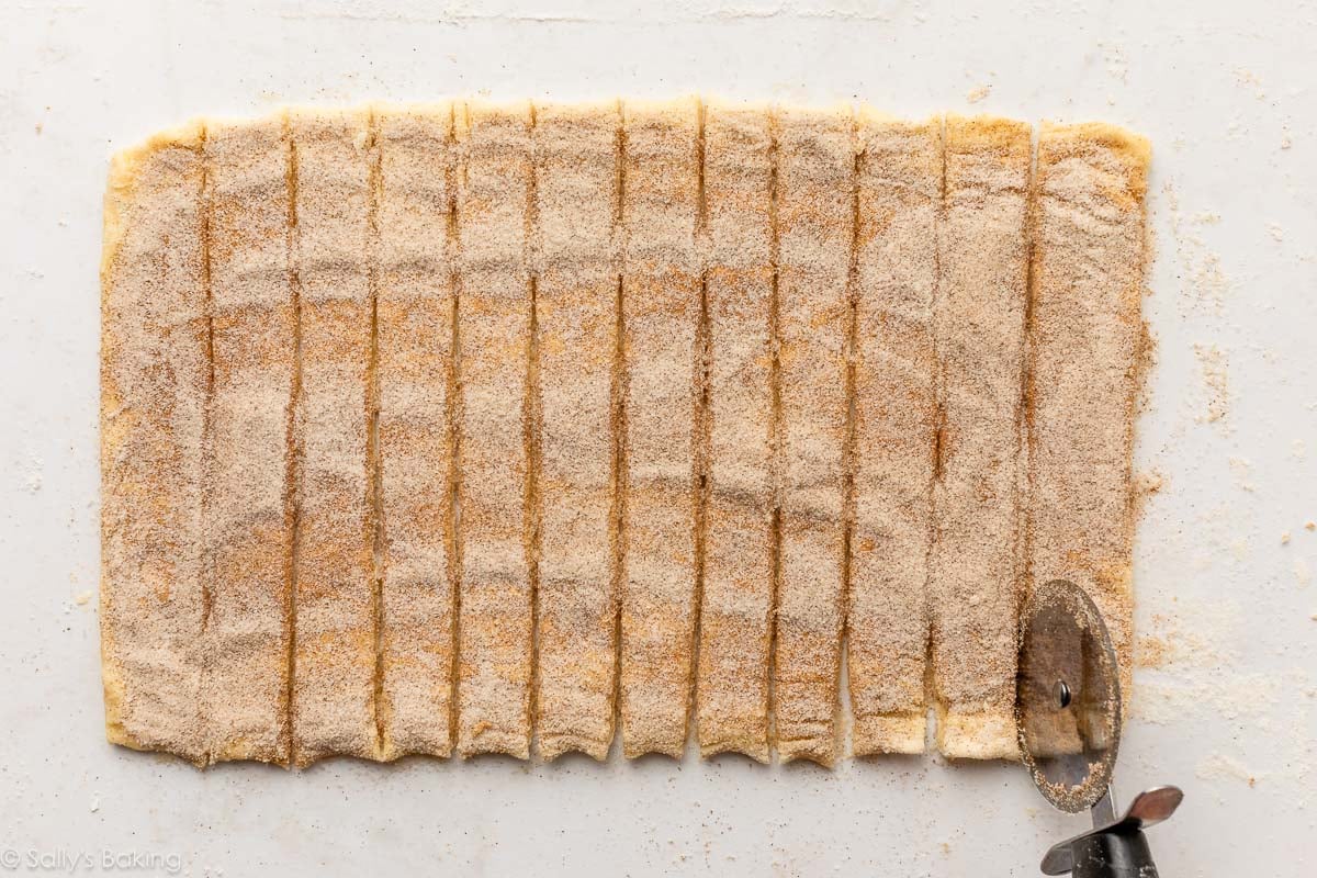 dough rolled out on surface covered in cinnamon sugar and cut into 12 strips.