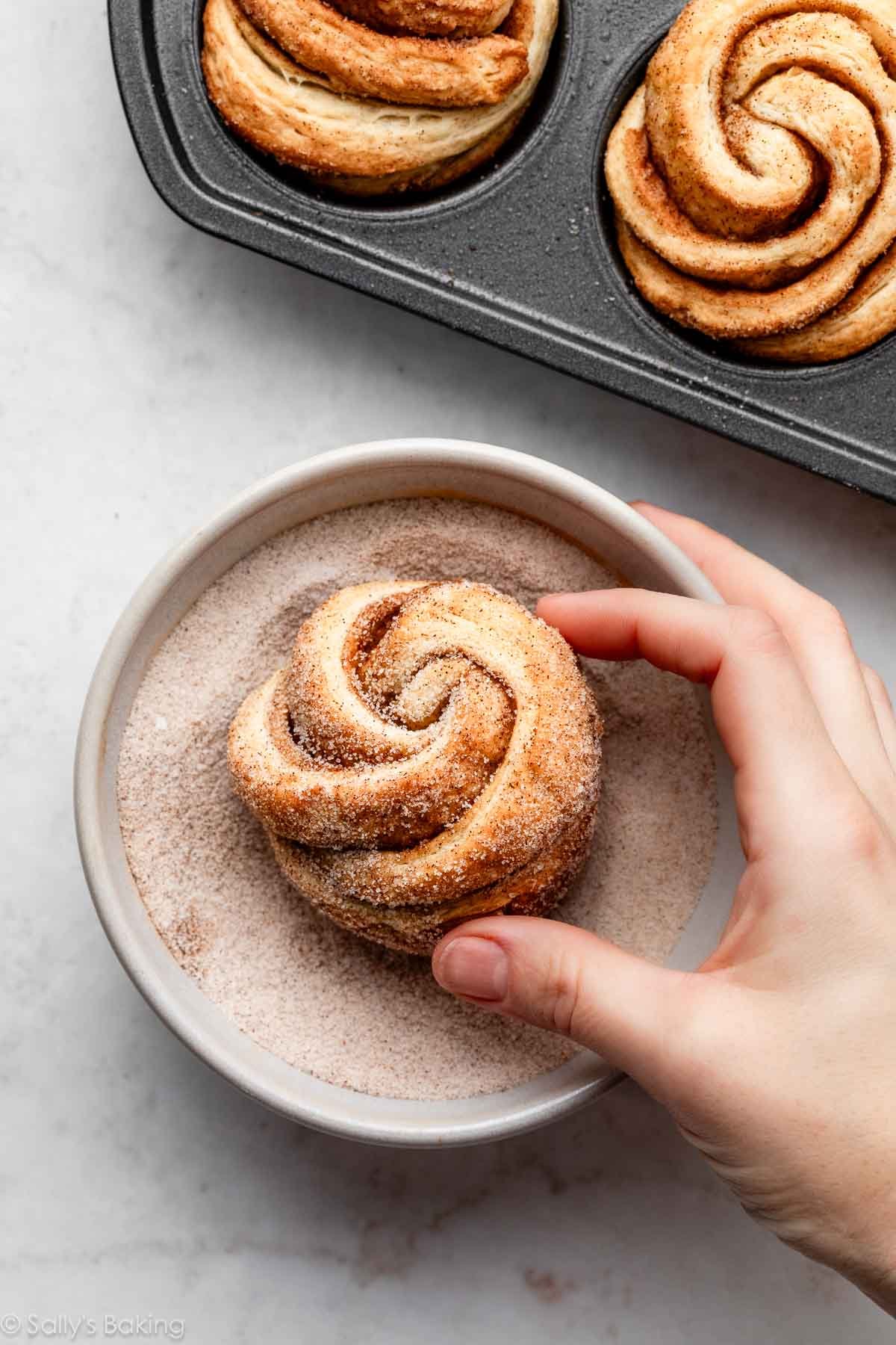 hands rolling cruffin pastry in cinnamon sugar.