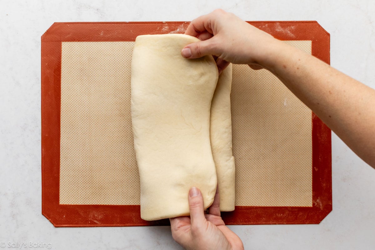 hands folding dough over lamination butter layer on top of silicone baking mat.