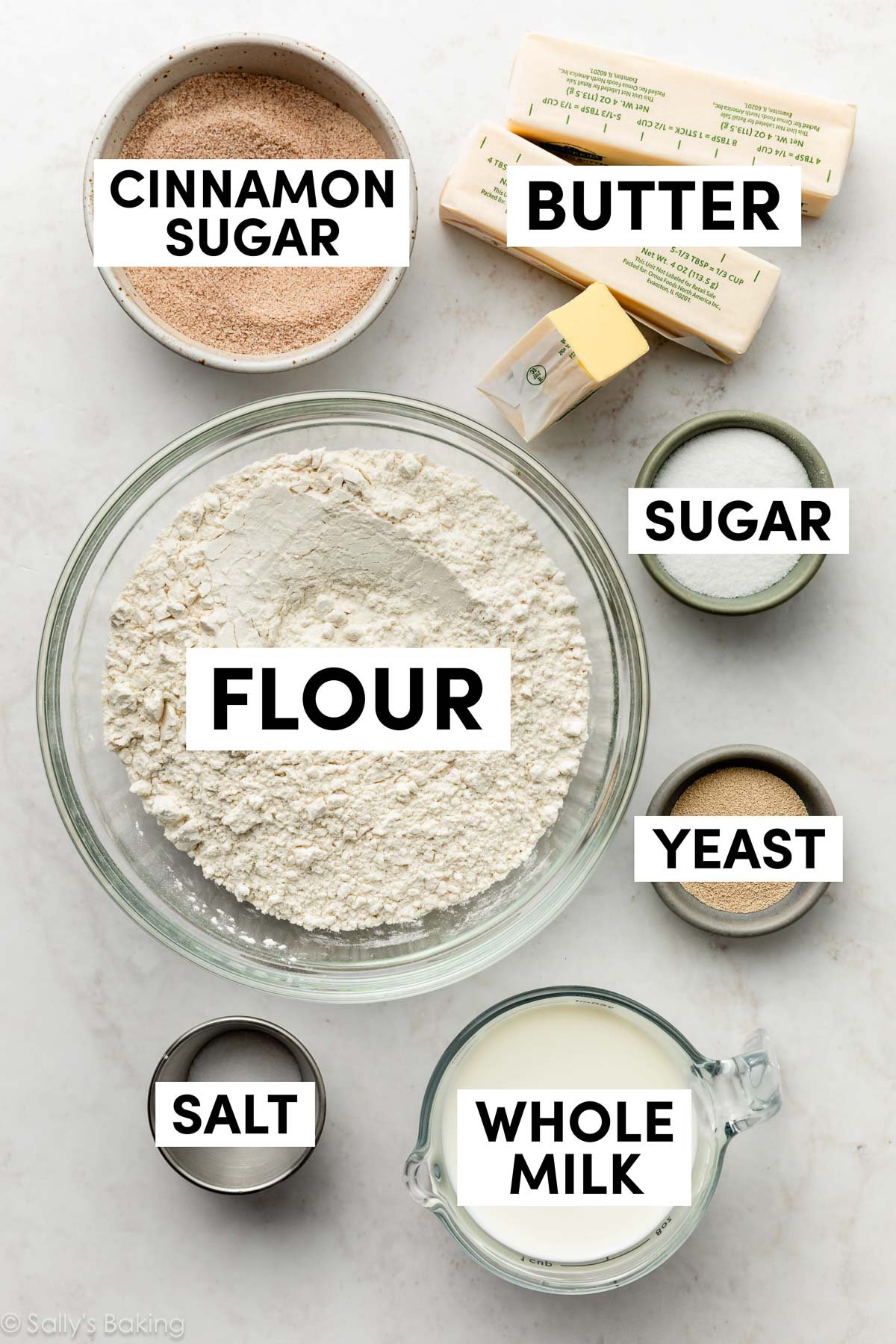 ingredients on marble surface including flour, butter, sugar, yeast, and milk.