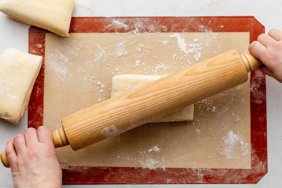 hands rolling small block of folded dough on silicone baking mat.