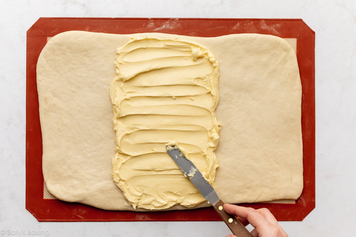 spreading butter on dough on top of silicone baking mat.